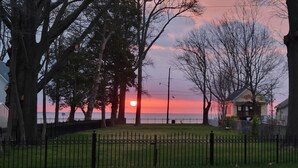 Un coucher de soleil sur une étendue d’eau, avec une zone herbeuse et une clôture au premier plan.