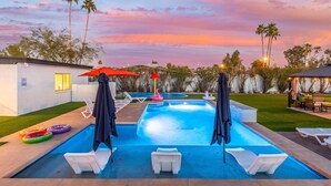 Una piscina con lettini e ombrelloni, circondata da palme e un cielo al tramonto.