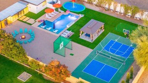 Una vista aerea di una proprietà residenziale con piscina, area salotto all'aperto, campo da basket e un piccolo padiglione.