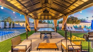 Area ricreativa all'aperto con tavolo da ping pong, poltrone relax e piscina.