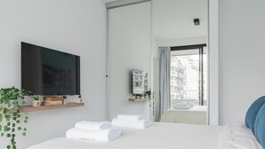 Et moderne hotelværelse med en seng, et fladskærms-tv, en lille hylde med planter og udsigt over byen gennem en glasdør.