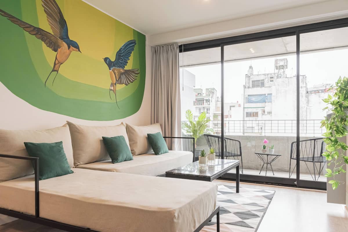 Habitación de hotel moderna con un ventanal grande, un sofá, una mesita y un balcón con sillas.