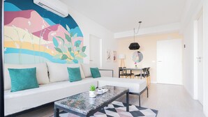 En moderne stue med en hvid sofa, turkise puder, et marmorbord og et farverigt mural på væggen.
