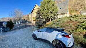 Une voiture blanche est garée sur une allée de gravier dans un quartier résidentiel, bordé de maisons et d’arbres.