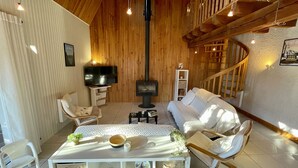 Un salon chaleureux avec un décor intérieur en bois, une télévision, une cheminée, un canapé et une table à manger avec des chaises.