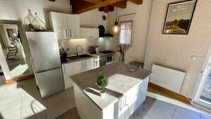 Une cuisine moderne avec des meubles blancs, un îlot central, un four encastré et un luminaire suspendu.