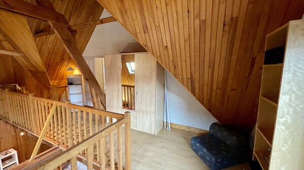 A wooden interior with a sloped ceiling, a staircase, and a sofa.