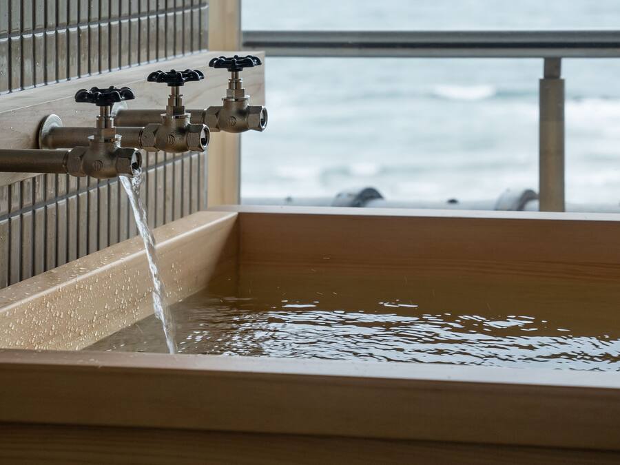 A wooden bathtub with a faucet, a window, and a view of the ocean.