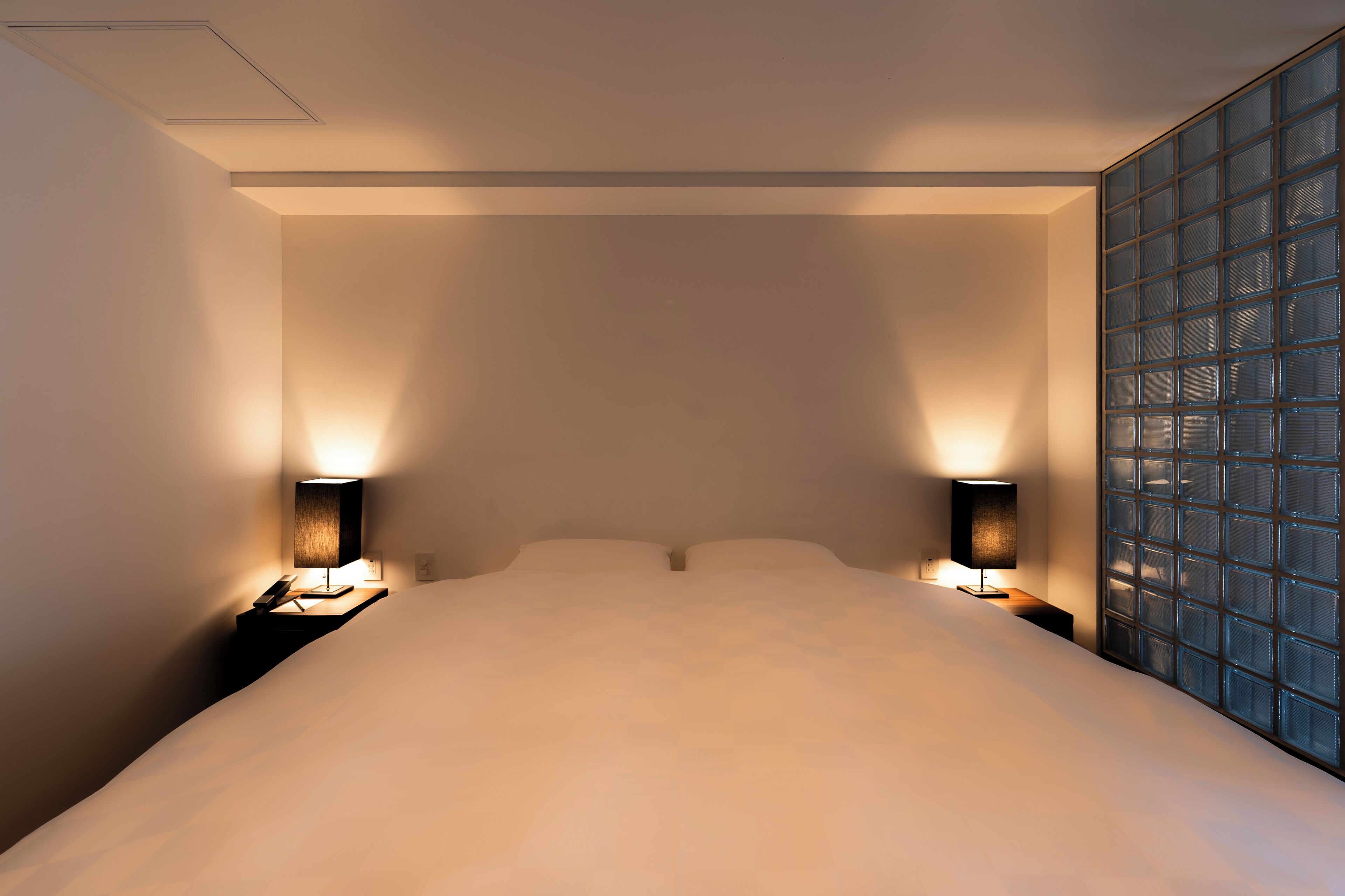 A hotel room with a large bed, two bedside lamps, and a view through a glass partition.