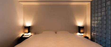 A hotel room with a large bed, two bedside lamps, and a view through a glass partition.