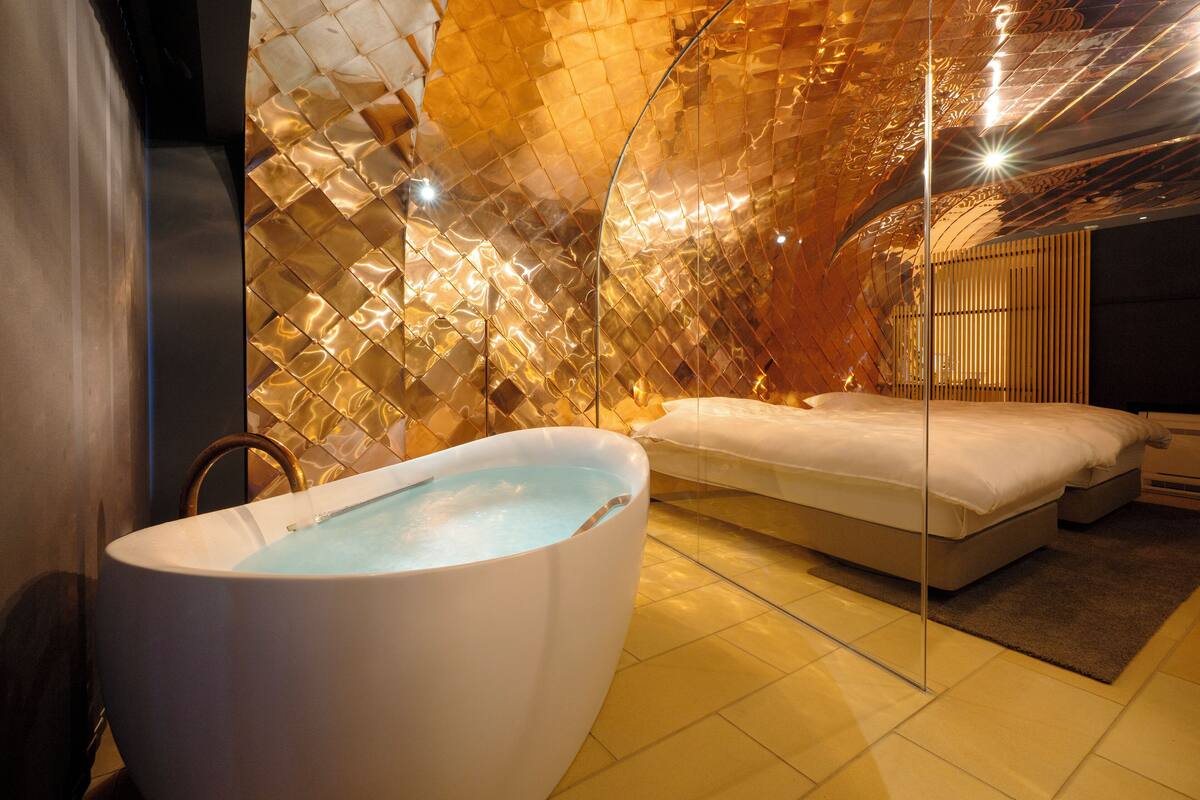 A modern bathroom with a large bathtub, a bed, and a unique textured wall.