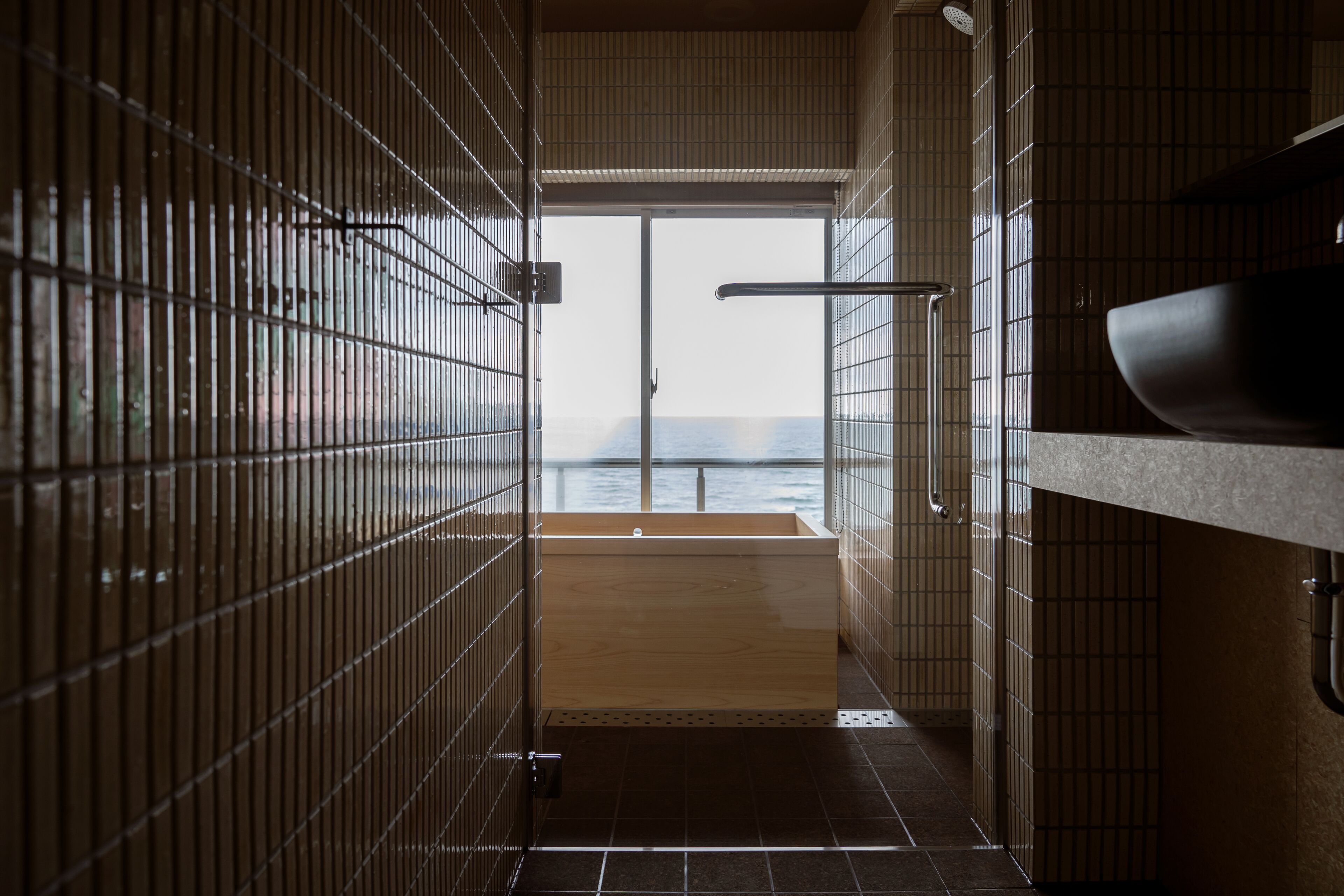 A modern bathroom with a large window, a wooden bathtub, and a sink.