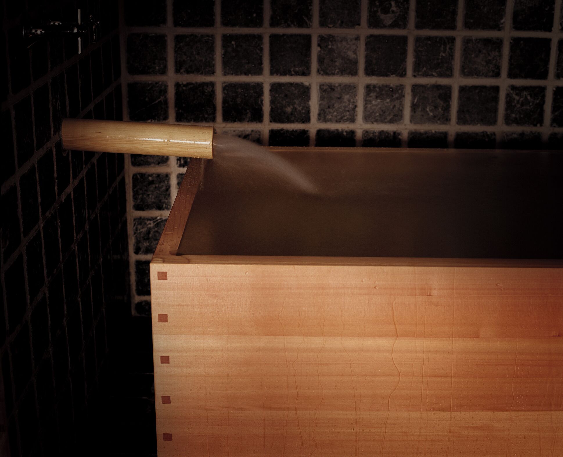 Una vasca da bagno in legno con un manico di legno, su uno sfondo di piastrelle.