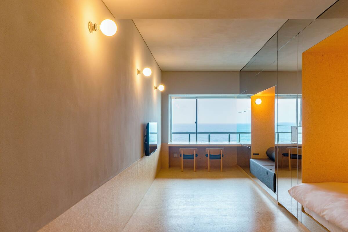 A modern hotel room with a large window, a bed, a desk, and two chairs.