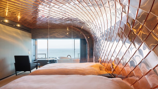 Una camera da letto moderna con soffitto curvo, un letto grande, una poltrona e vista sul mare.