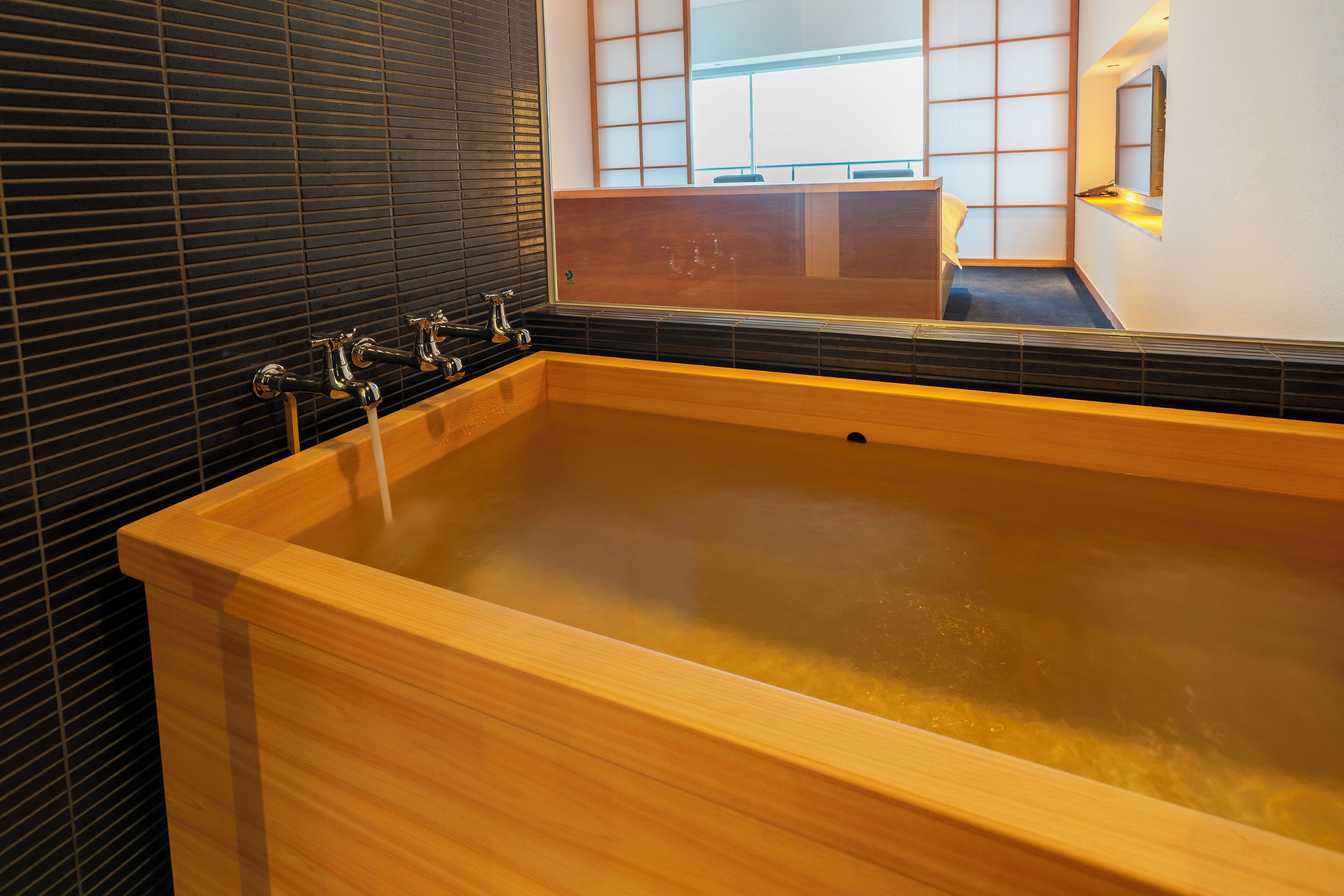 A large wooden bathtub with a wooden bench, a mirror, and a window with blinds.