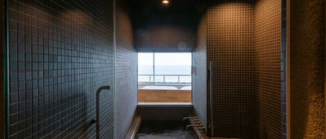 A narrow, tiled room with a bench and a view of the sea through a window.