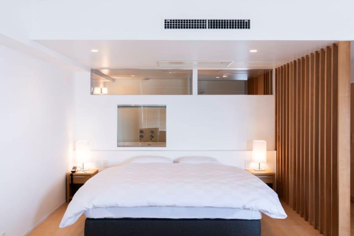 Een moderne hotelkamer met een groot bed, twee nachtkastjes, een spiegel en een wandpaneel van hout.