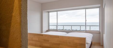 A bedroom with a large window overlooking the sea, a wooden bed, and a tatami mat floor.