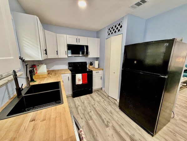A compact kitchen with white cabinets, a black refrigerator, a microwave, and a stove.
