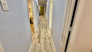 A narrow hallway with light blue walls, wooden flooring, and white trim.