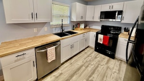 A modern kitchen with white cabinets, a black stove, and a wooden countertop.