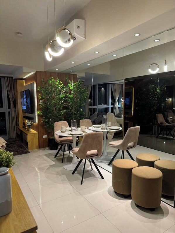 A modern dining area with round tables, cushioned chairs, and a large potted plant. - Modern Stylish 1BR Condo Uptown BGC w/ View - 22u (Taguig)