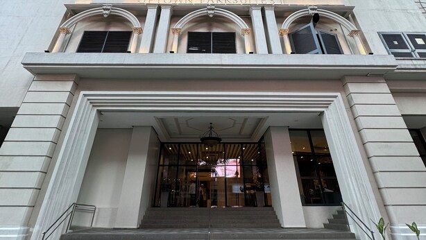 A building with a grand entrance, multiple floors, and a modern glass facade in the background.