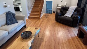 Een ruime woonkamer met een houten vloer, een bank, een salontafel en een trap naar een hoger gelegen verdieping.