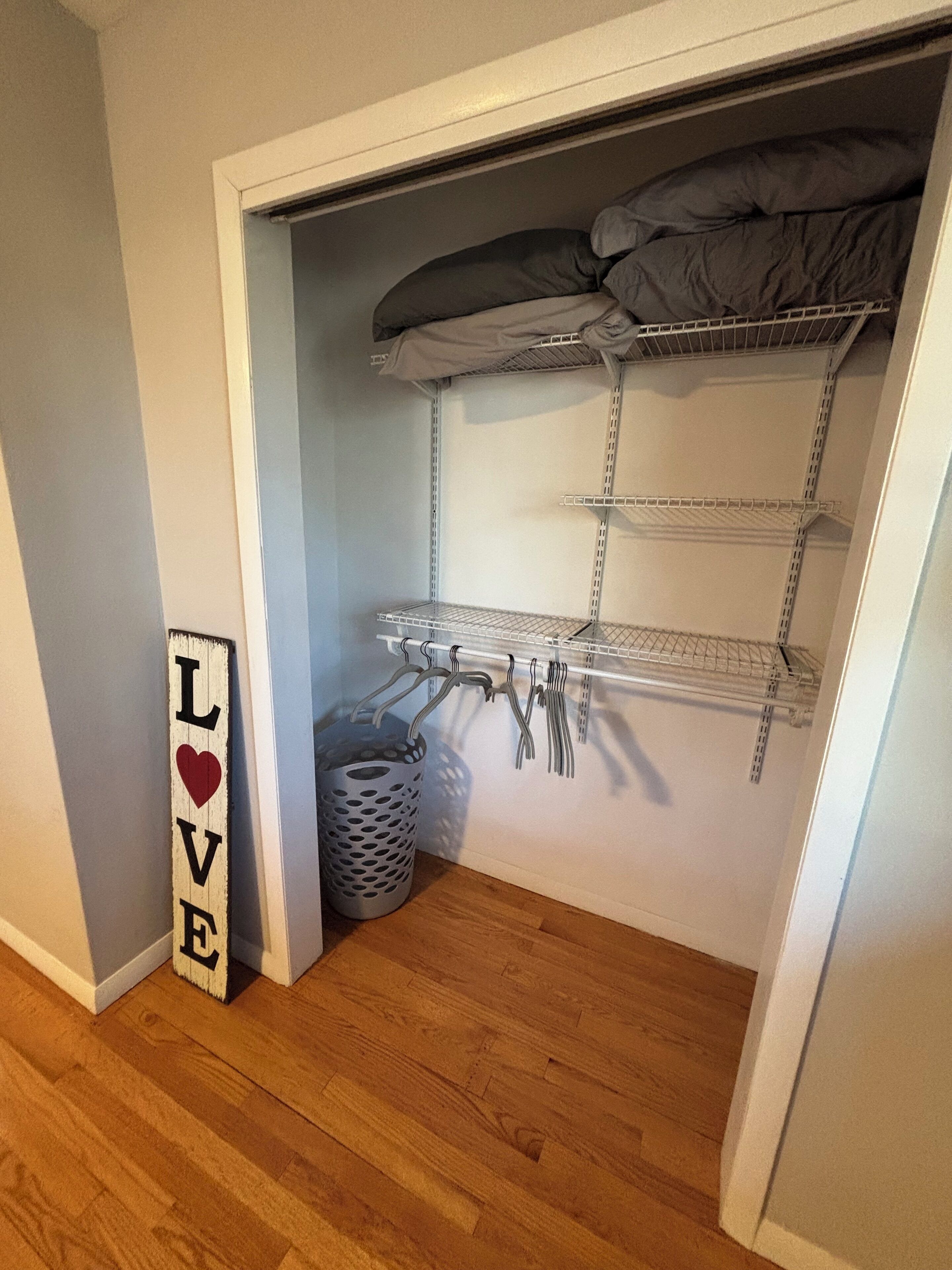Ein Schrank mit Regalen und Kleiderstange, ein grauer Korb und ein Schild mit der Aufschrift 'LOVE'.