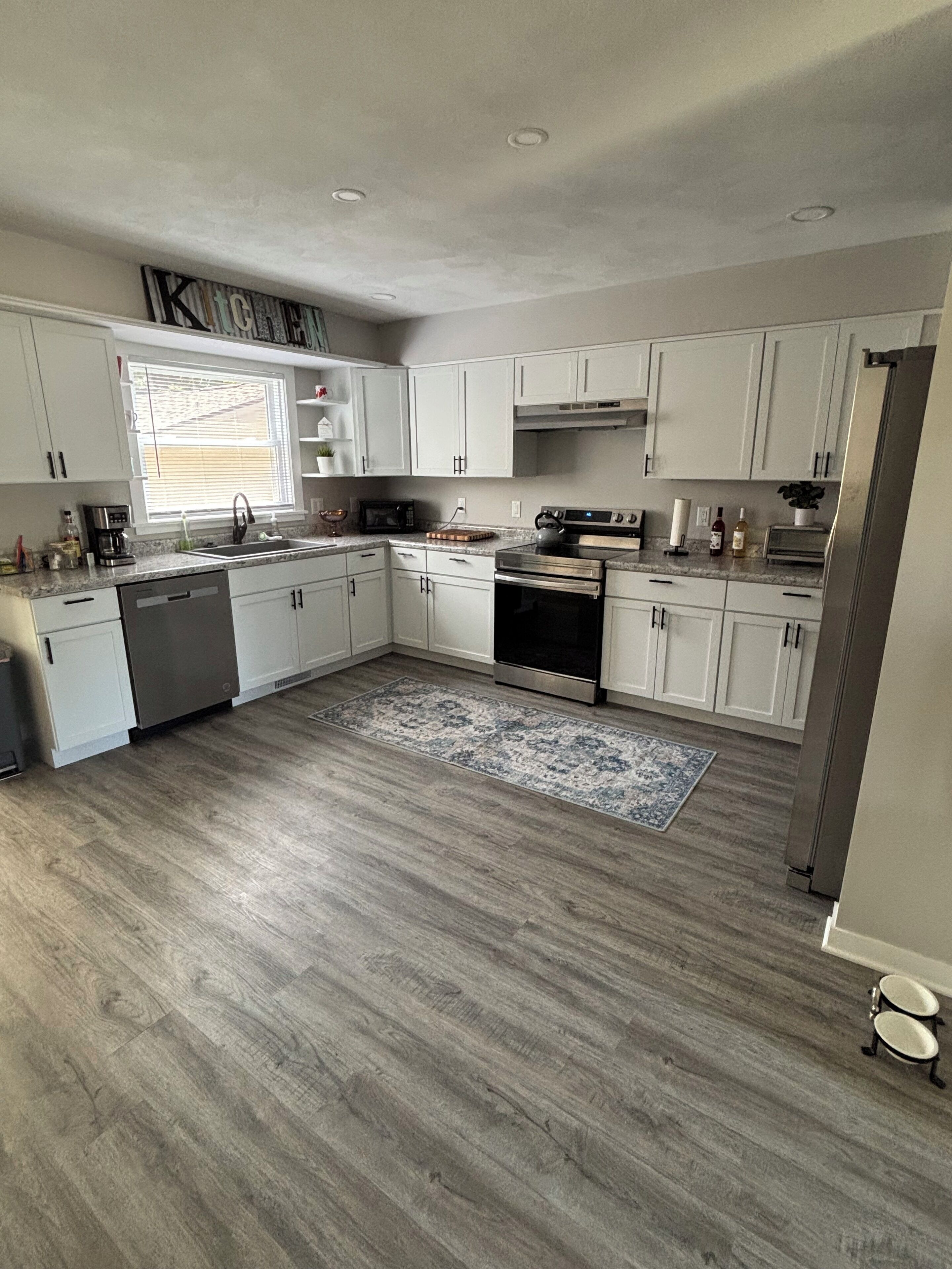 Una cocina moderna con armarios blancos, una estufa de acero inoxidable y piso de madera.