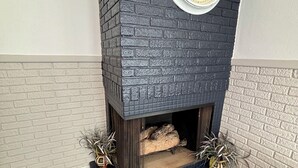 Een open haard met erboven een ronde klok, geplaatst in een hoek met een bakstenen muur en houten vloer.