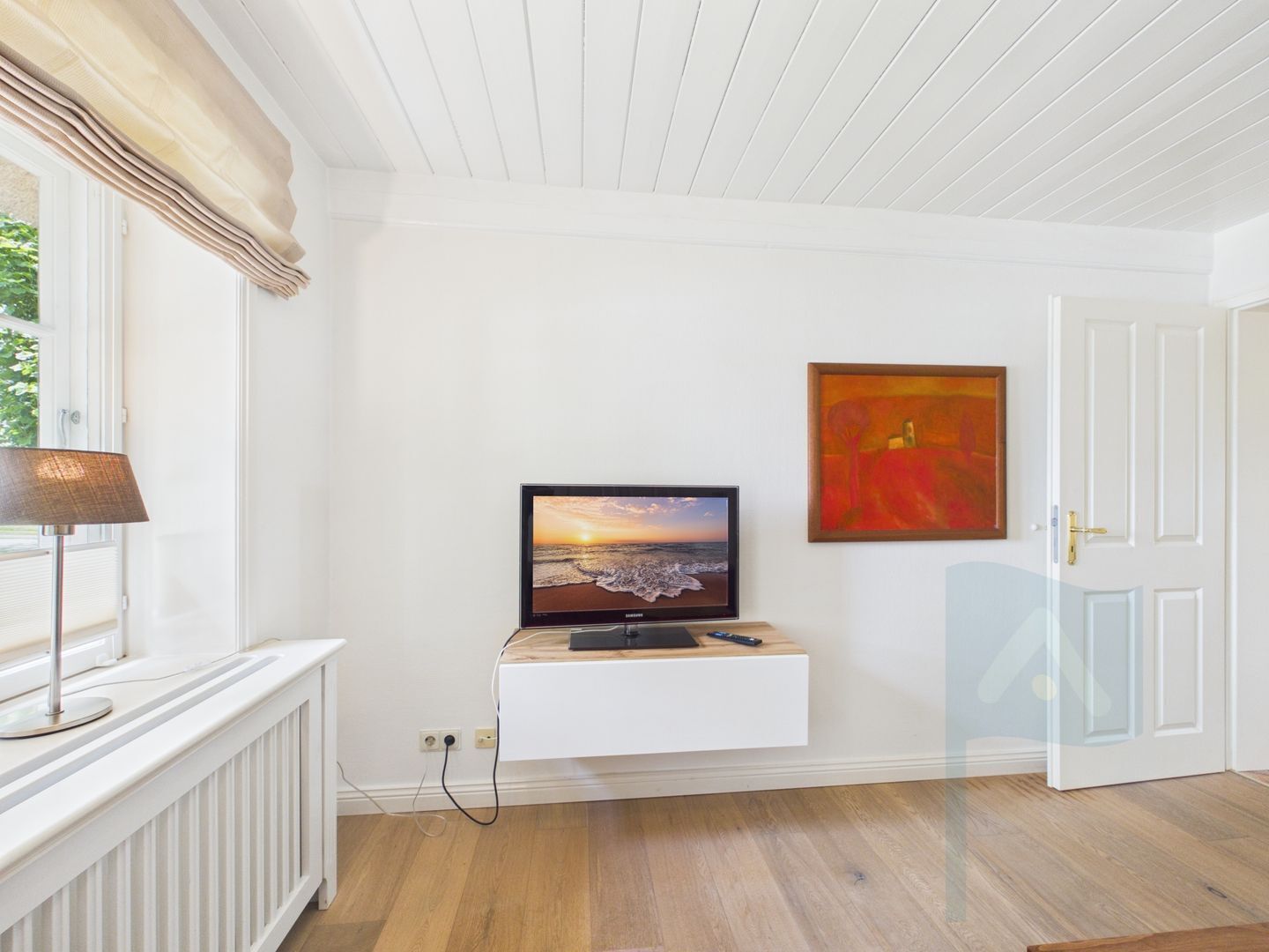 A room with a mounted TV on a white wall, a door, and a window with a lamp.