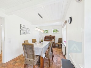 Ein Essbereich mit einem Tisch für vier Personen, umgeben von Korbstühlen, einem Holzschrank und einer Heizung.