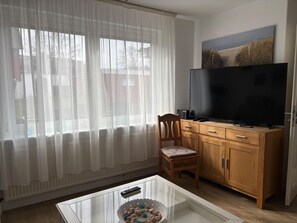Una sala de estar con televisor, aparador de madera y una silla.