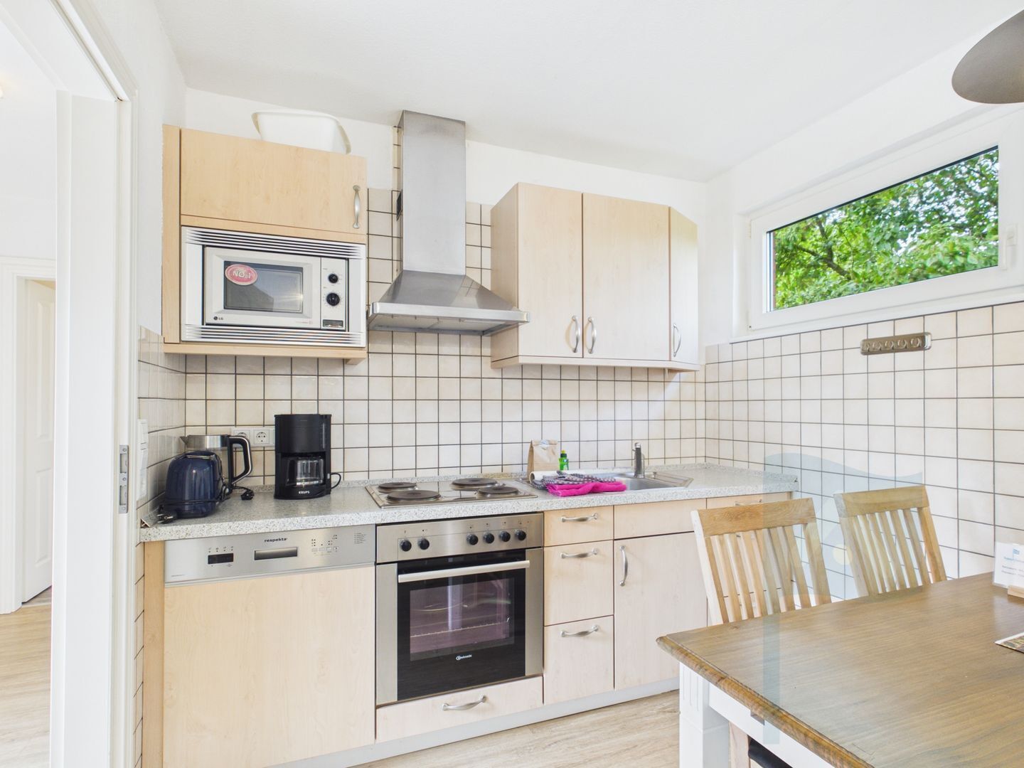 A compact kitchen with a microwave, stove, oven, and a window with a view of greenery.