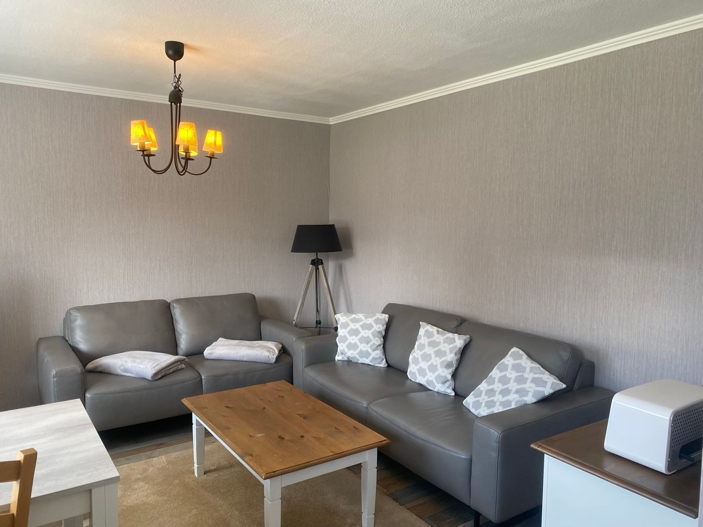 Ein modernes Wohnzimmer mit einem grauen Sofa, einem Holztisch, einer Lampe und einer Deckenleuchte.
