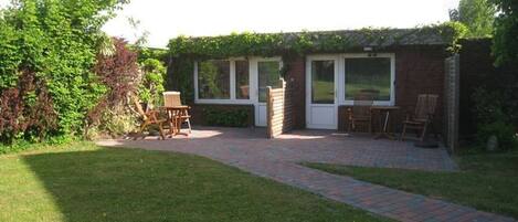 A brick patio with a grassy lawn, a wooden chair, and a table.