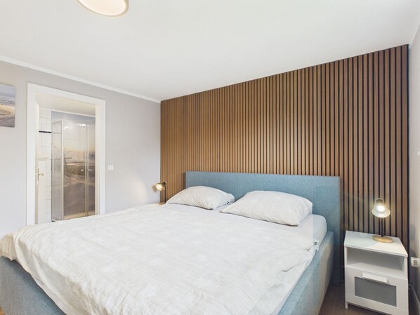 A bedroom with a bed, bedside tables, a wooden panel wall, and a door leading to a balcony.