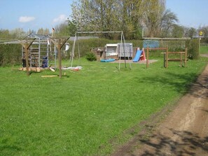A grassy area with a metal structure, possibly a play area, and a dirt path alongside.