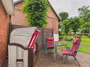 A patio with wicker chairs, a metal table, and a brick wall.