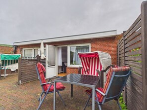 Eine Terrasse mit Tisch und Stühlen, ein überdachter Sitzbereich und ein Backsteinhaus mit Schiebetür.