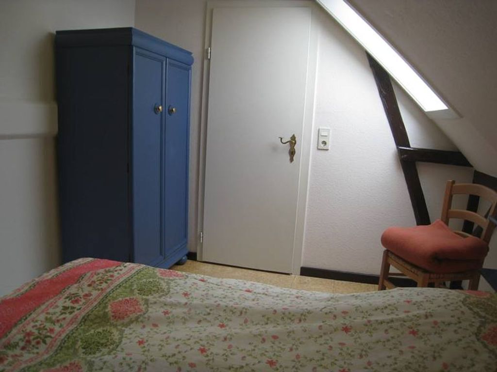 A bedroom with a bed, a wardrobe, a chair, and a door.