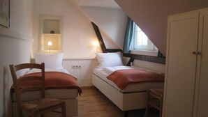 Et lille, hyggeligt værelse med to senge, en træstol, et skrivebord med lampe og et garderobeskab.