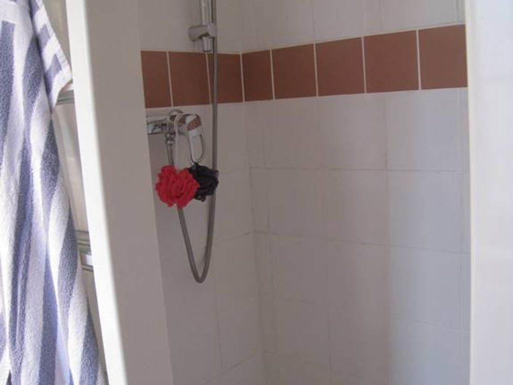 Een douchegedeelte met een witte betegelde muur, een douchekop en een rode handdoek aan een rek.