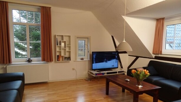 En stue med fjernsyn, et sofabord med blomster, en sort sofa og en bogreol.