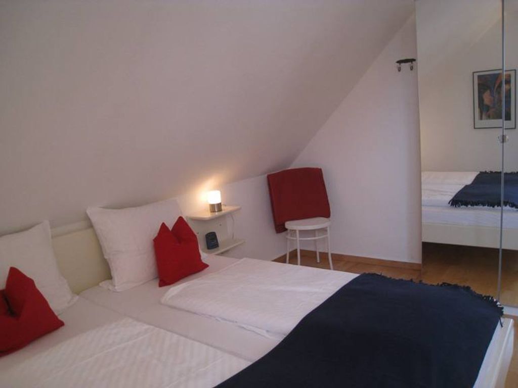 Une chambre à coucher avec un lit, une table de chevet avec une lampe, une chaise et un lit en arrière-plan.