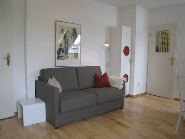 A modern living room with a grey sofa, a small white side table, and a framed picture on the wall.
