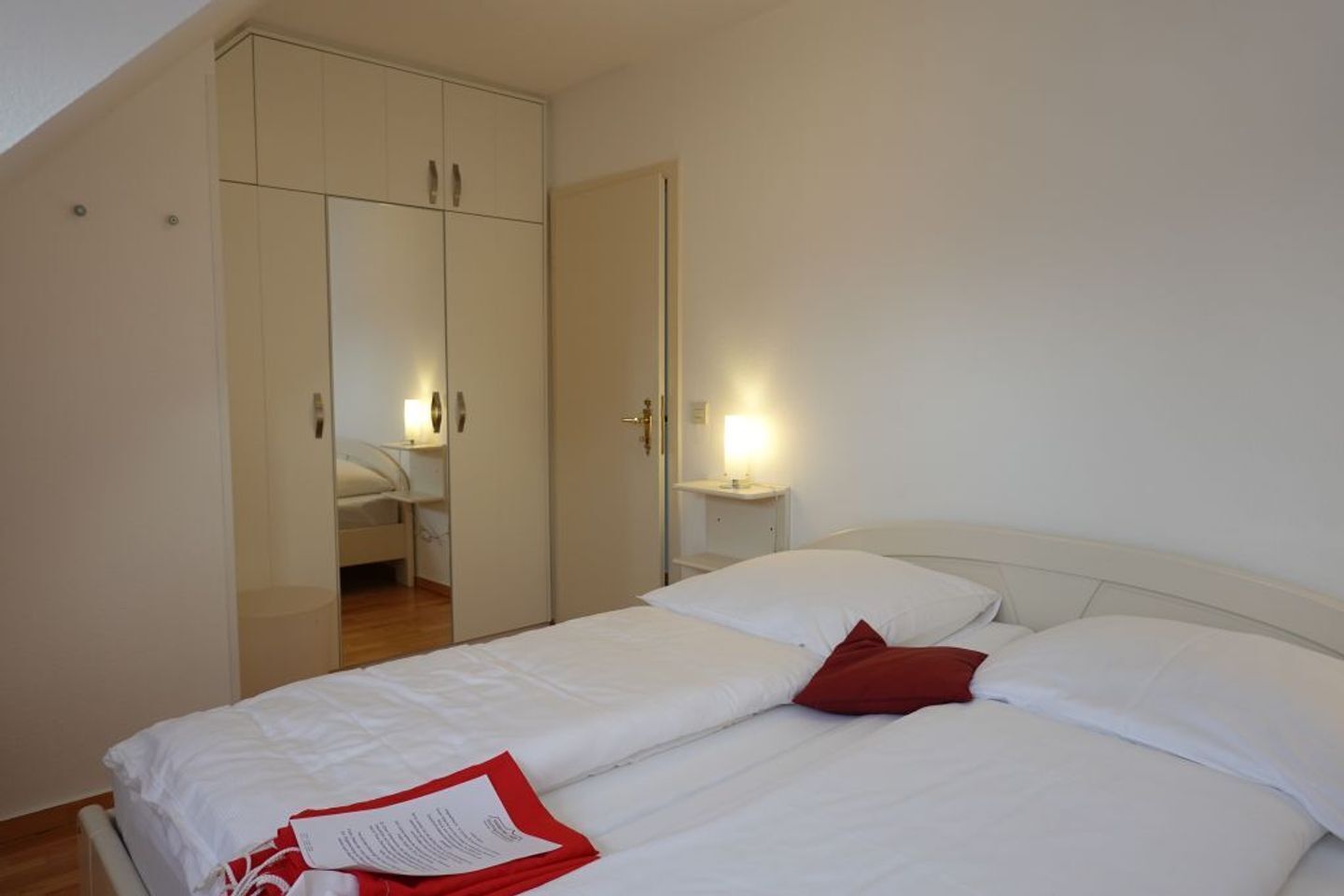 A bedroom with a bed, a wardrobe, and a nightstand with a lamp.