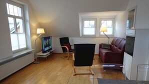 Uma sala de estar moderna com televisão de tela plana, uma cadeira preta, um sofá vermelho e uma mesa de centro de vidro.
